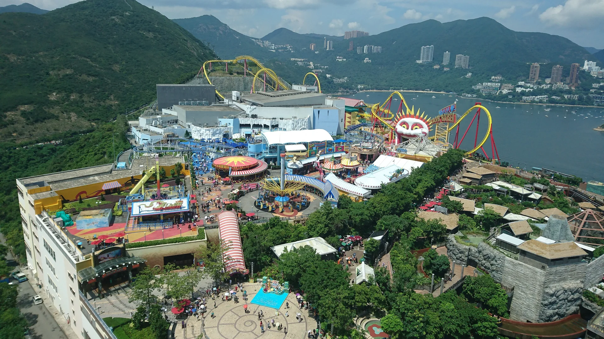 Η περιοχή Summit του Ocean Park Hong Kong από ψηλά, με τρενάκια δίπλα σε έναν κόλπο και καταπράσινα βουνά στο βάθος